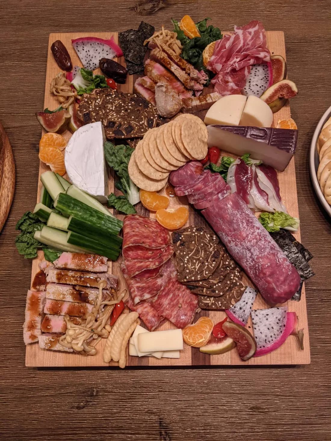 A grazing board with seared tuna in a soy glaze and enoki mushrooms beside cured meats, cheeses, figs, dragon fruit, mandarins and nori